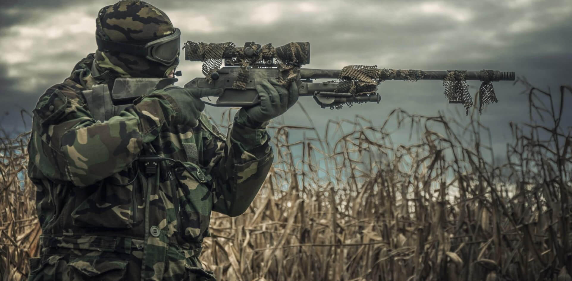 hombre con un rifle de francotirador apuntando hacia la izquierda con un camuflaje que simula la vegetacion que tiene alrededor de el