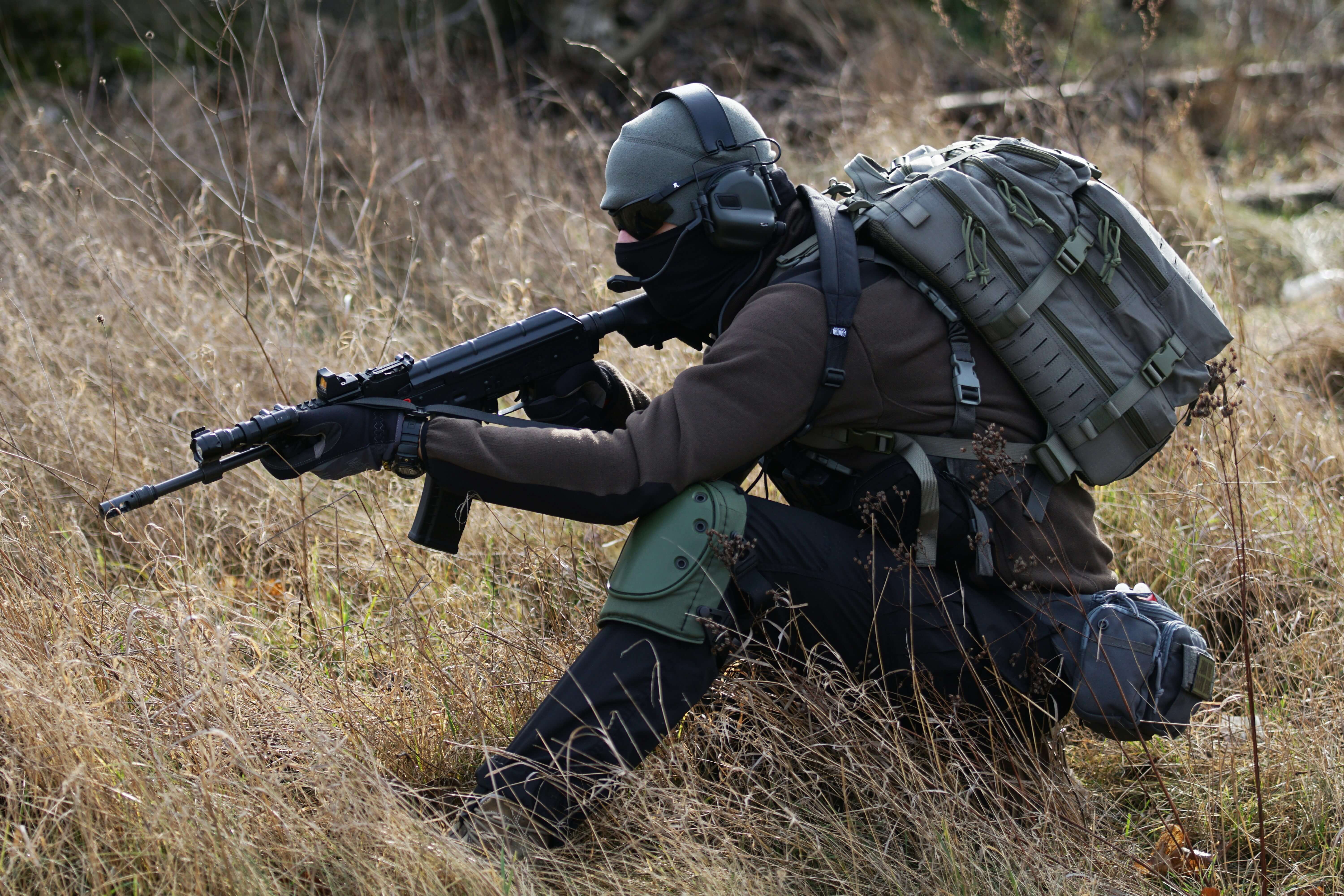 hombre agachado con todo su equipaje y su fusil de asalto con la guardia baja 